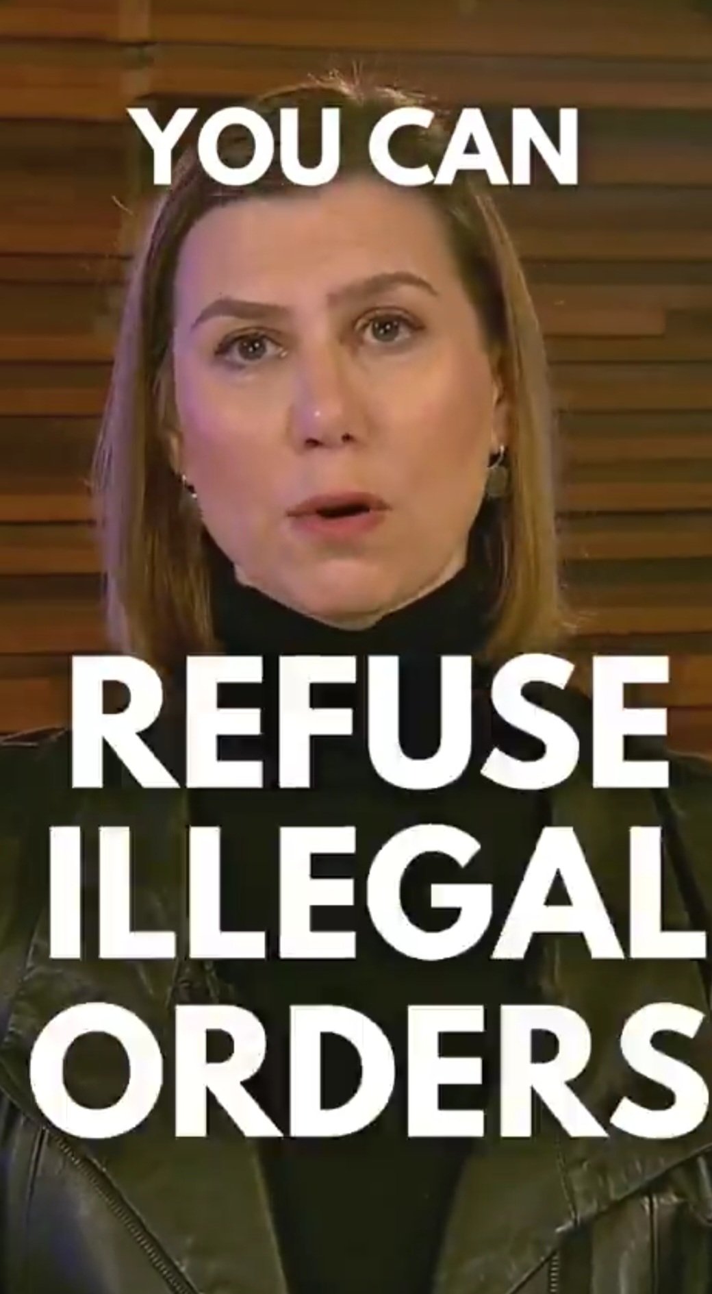 Woman speaking about the importance of refusing illegal orders, wearing a black turtleneck and leather jacket, with a wooden background.