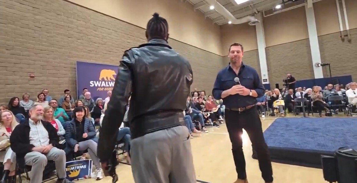 Audience engagement event featuring a speaker and attendees, with a backdrop promoting Swalwell for Governor campaign.