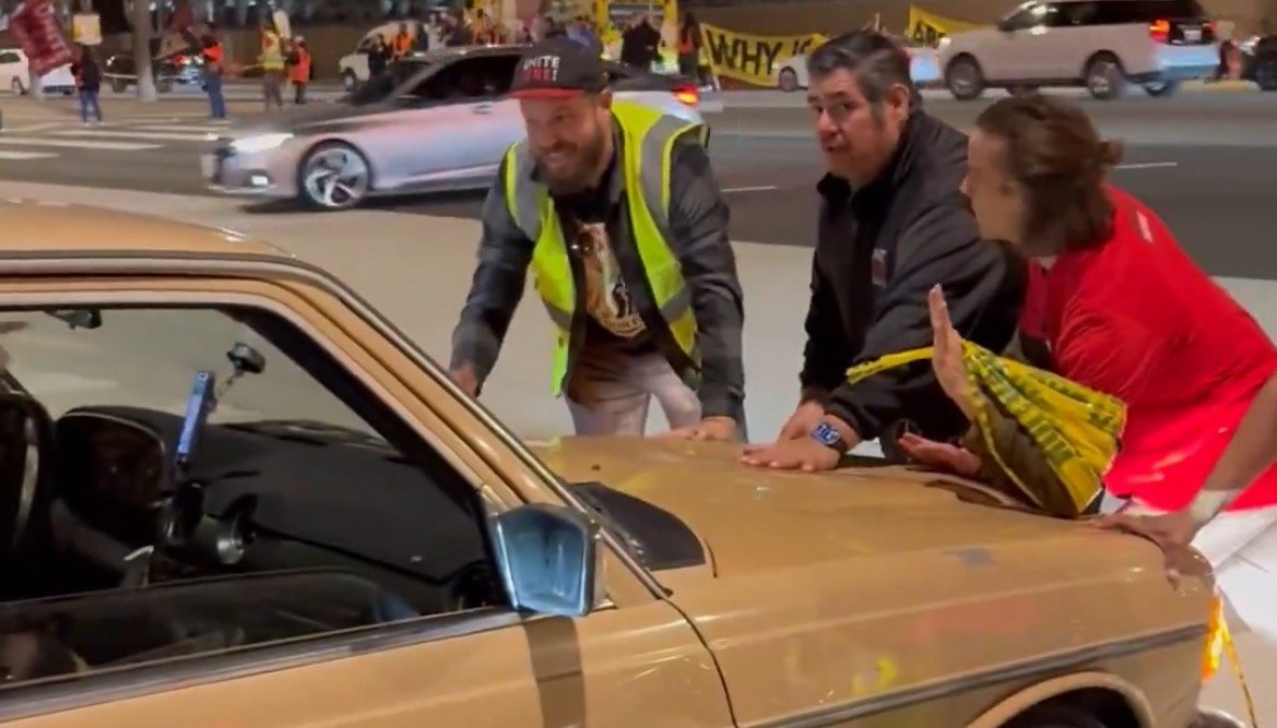 Protesters engaging with a car during a demonstration, showcasing community involvement and activism in a public setting.