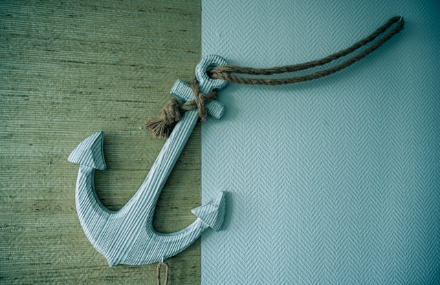 A white necklace in the shape of an anchor, on a wooden surface. 