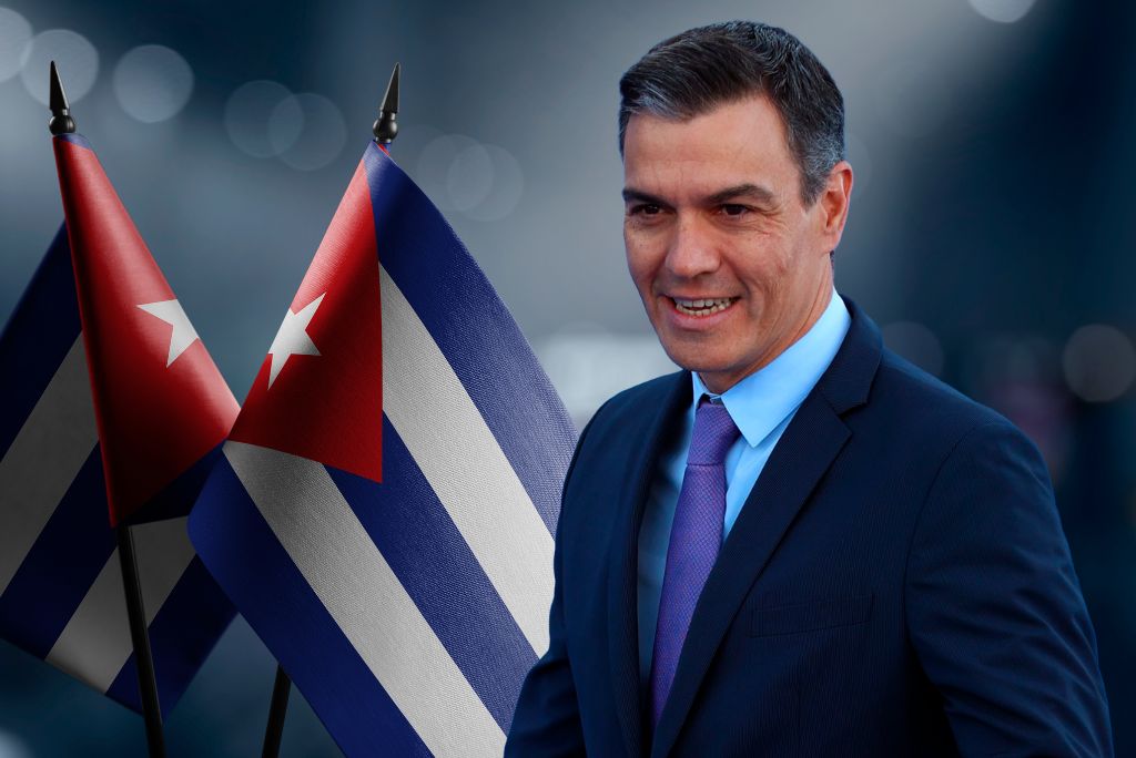 Smiling man in a suit stands in front of Cuban flags, symbolizing diplomatic relations or cultural ties between countries.
