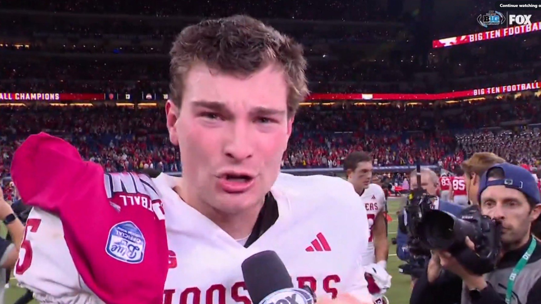 Indiana football player giving an interview after a victory, celebrating in front of a cheering crowd in a stadium.