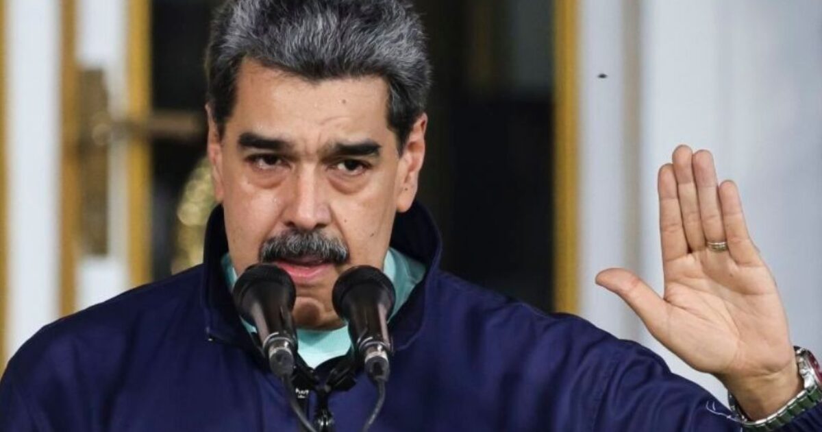 Venezuelan President Nicolas Maduro addresses the audience with a raised hand during a public speech, emphasizing his message at a podium.