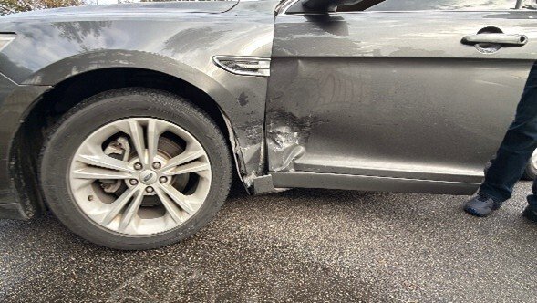Close-up of a damaged gray car door with visible dents and scratches, showcasing the impact on the vehicle's side.