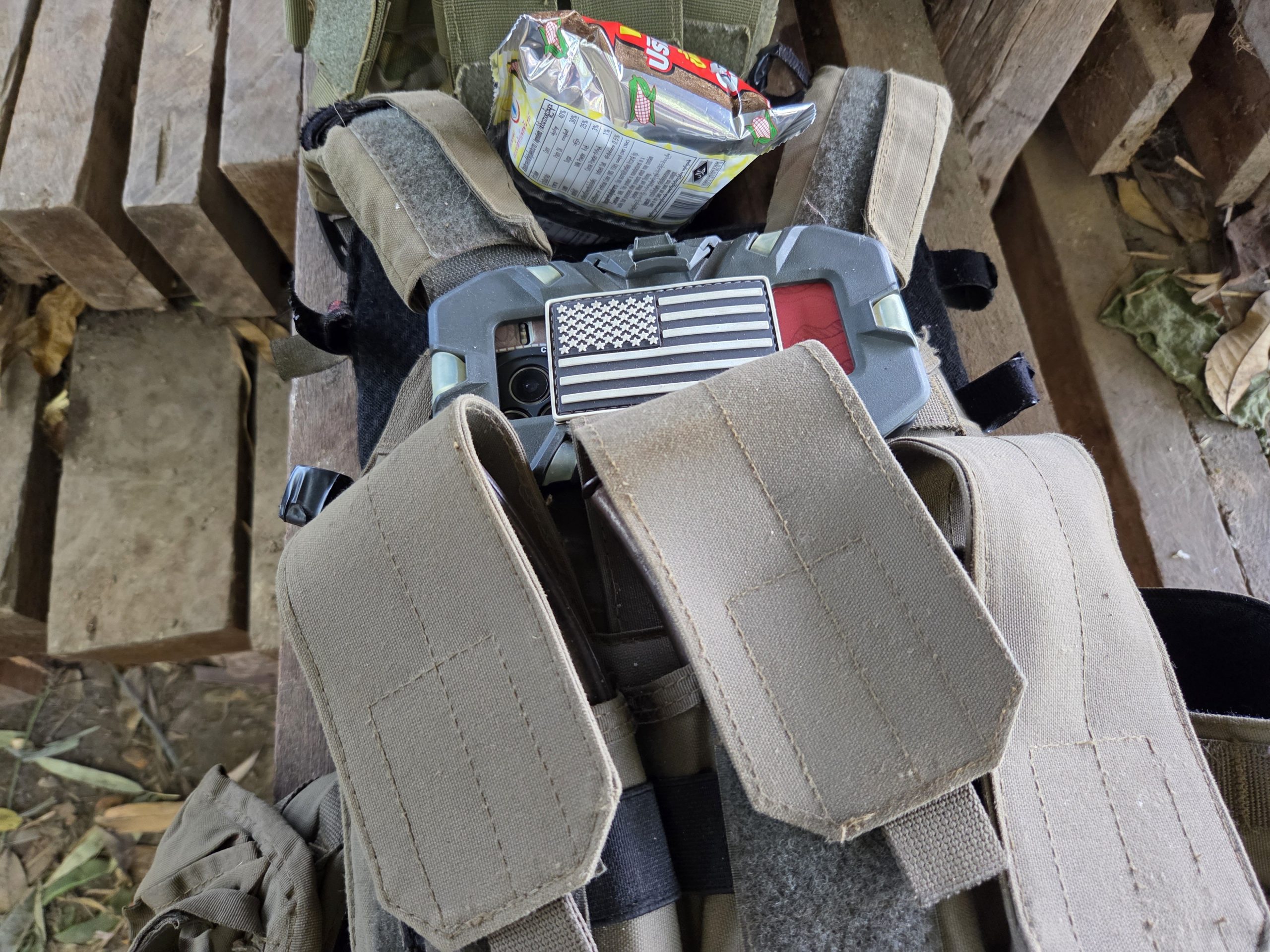Close-up of tactical gear featuring a phone with an American flag case, snack packaging, and a wooden surface in the background.