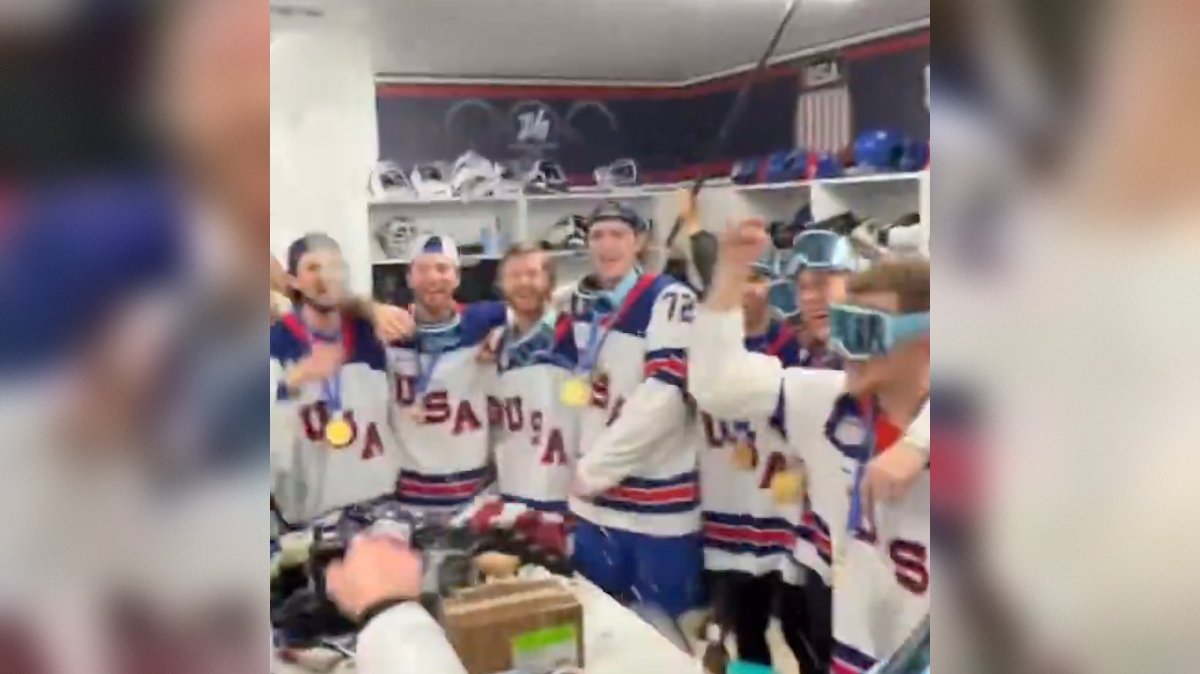 Celebrating hockey team members in USA jerseys with medals, joyfully posing in a locker room after a victory.