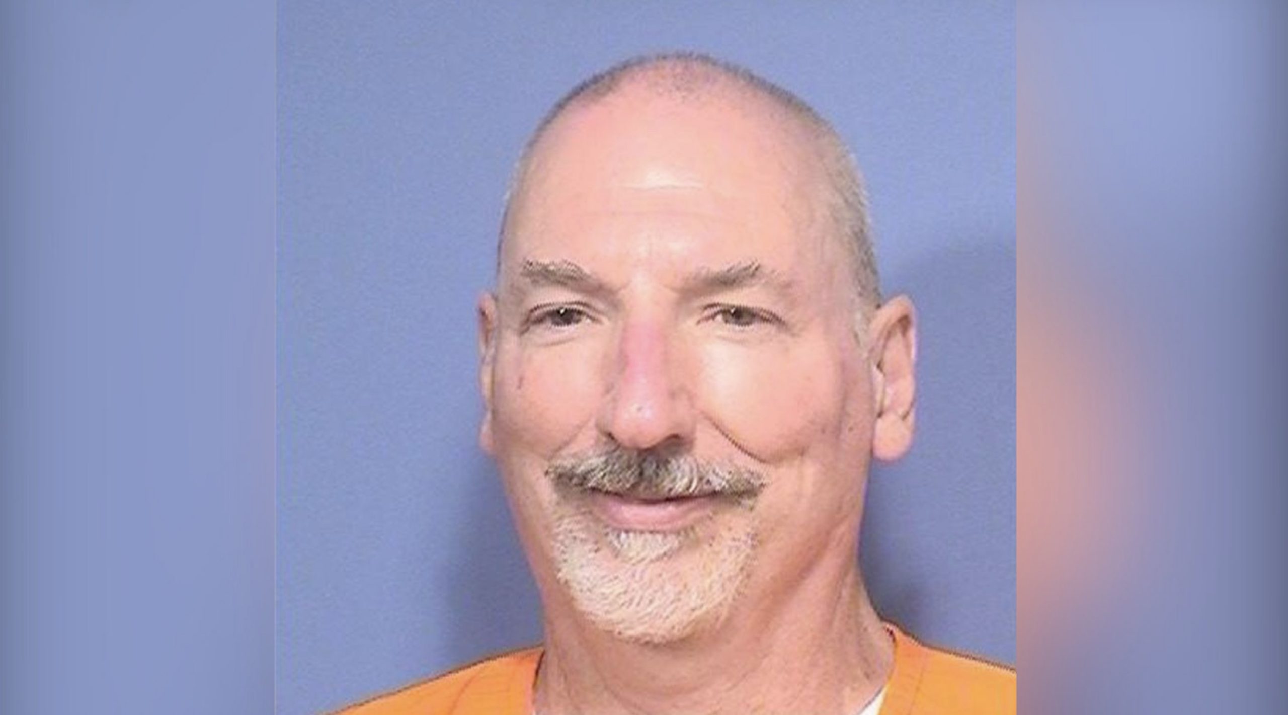 Inmate portrait of a middle-aged man with a mustache, wearing an orange jumpsuit against a blue background.