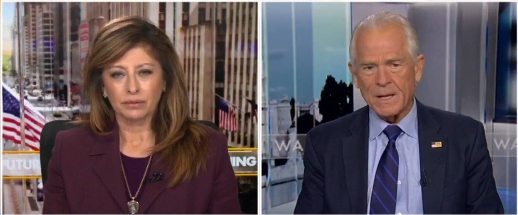 News interview featuring a female host and a male guest discussing current events, with a backdrop of urban scenery and American flags.