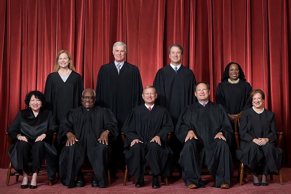 U.S. Supreme Court justices posing for an official group portrait, featuring nine members in black robes against a red curtain backdrop.