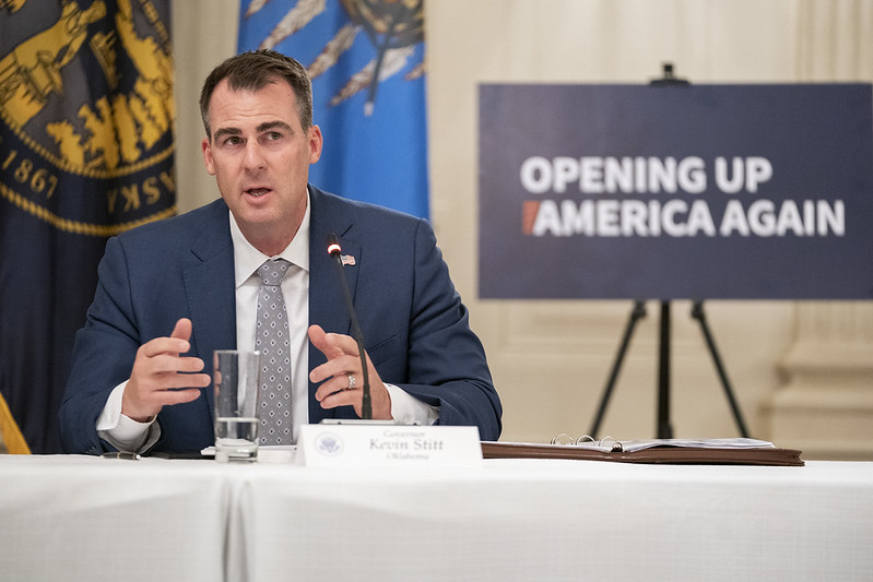 Oklahoma Governor Kevin Stitt speaks at a press conference about reopening strategies in front of a sign reading "Opening Up America Again."