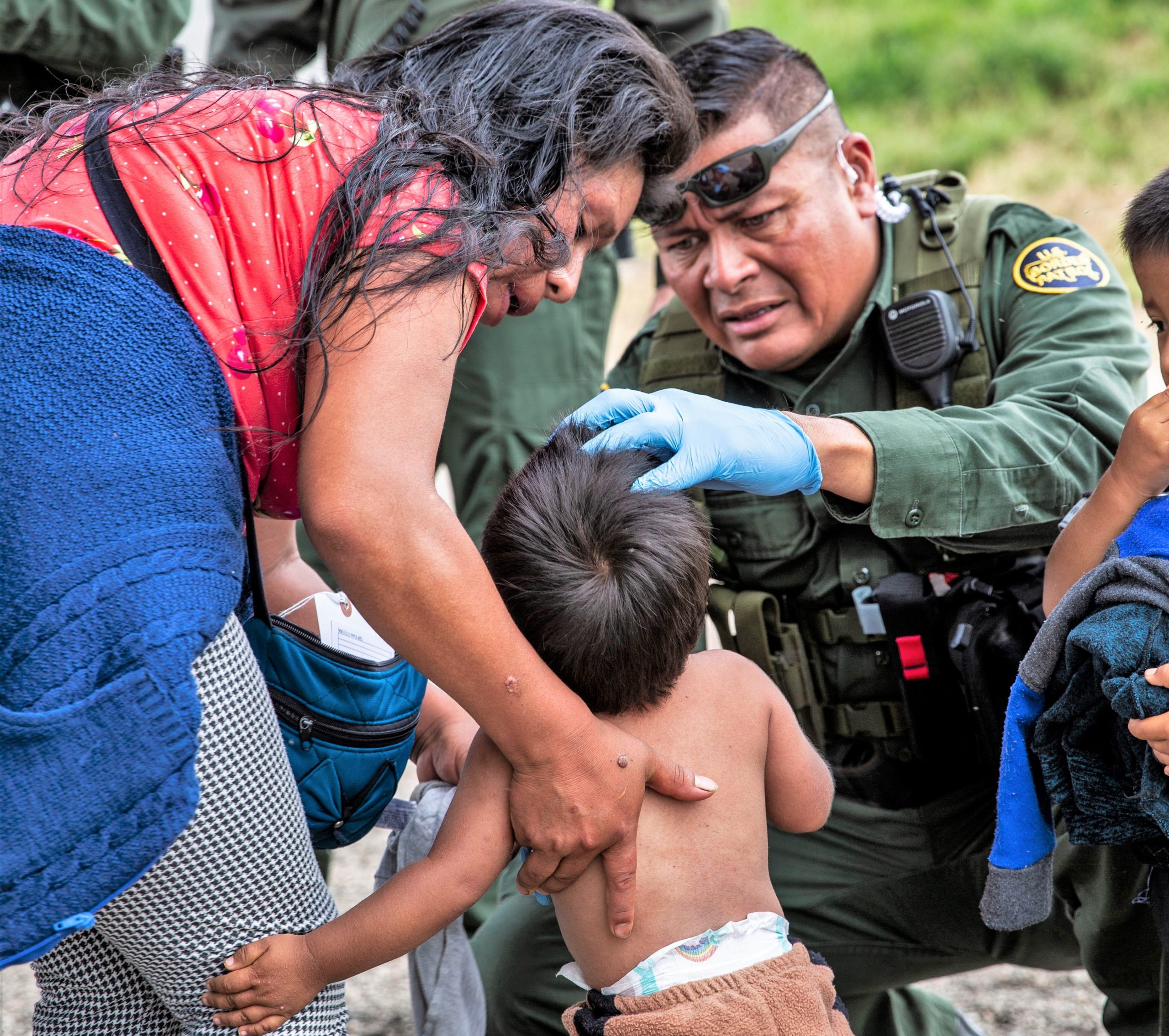 Border patrol officer assisting a mother and her young child during a humanitarian situation, demonstrating care and support in a challenging environment.