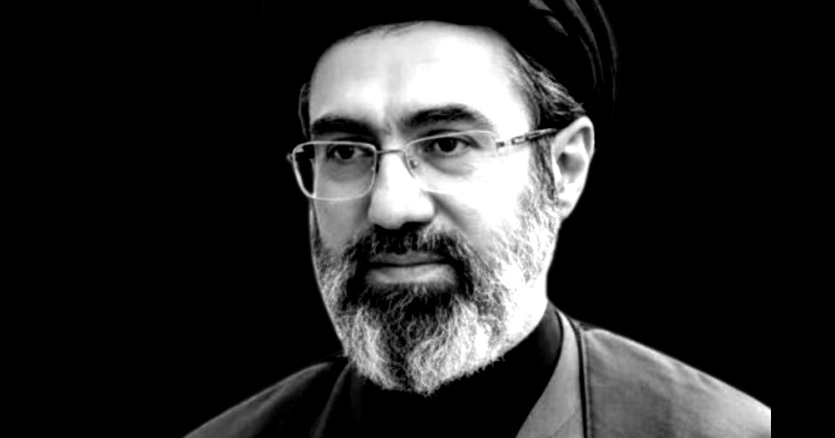 Portrait of a man with a beard and glasses, wearing a traditional black turban, set against a dark background.