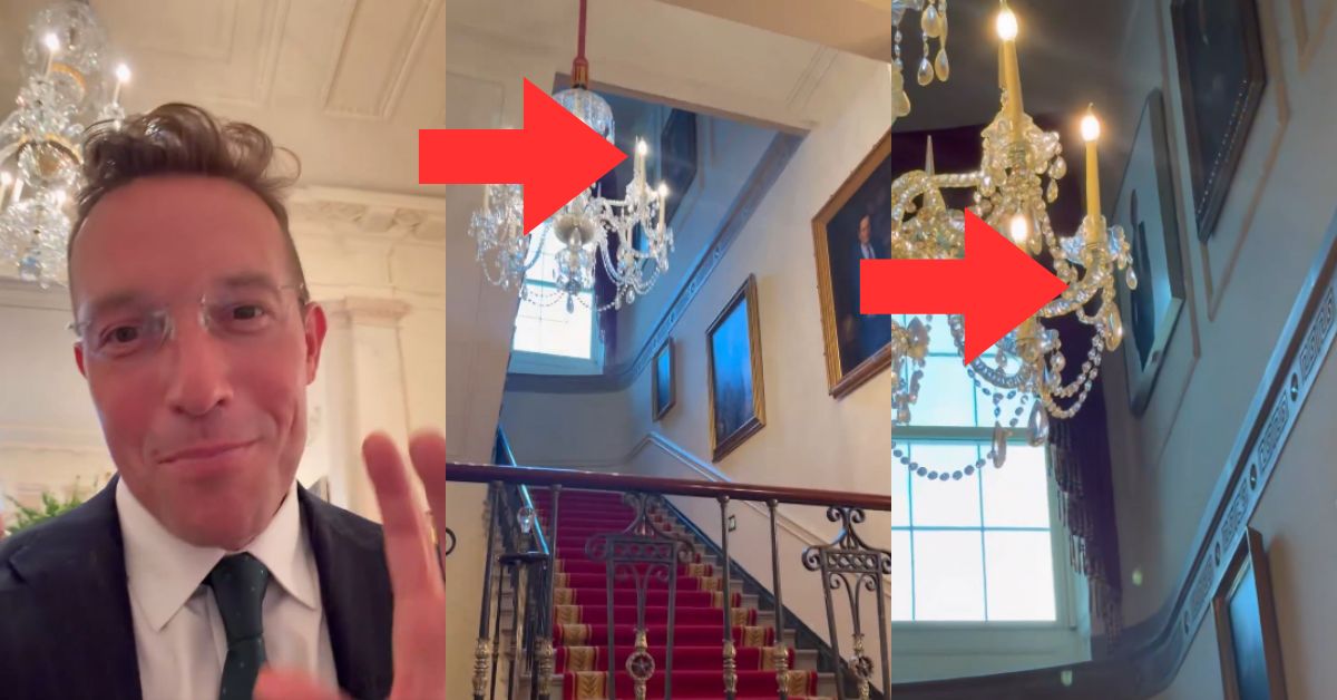 Man in a suit gestures while showcasing elegant chandeliers in a grand staircase setting, highlighting ornate decor and historical paintings.