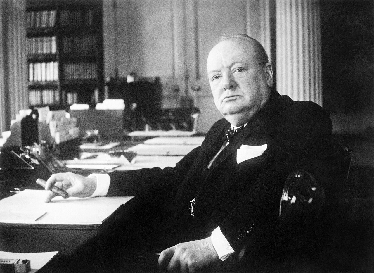 Portrait of a distinguished man in formal attire seated at a desk, surrounded by paperwork and books, exuding an air of authority and contemplation.