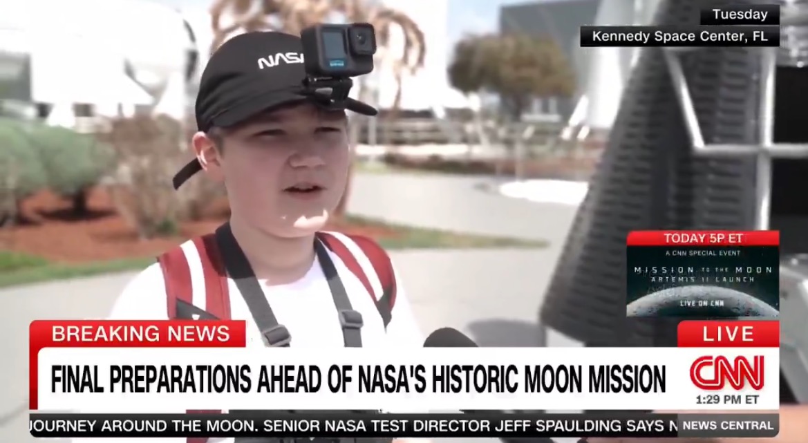 Young boy wearing a NASA cap and camera speaks about preparations for NASA's upcoming moon mission at Kennedy Space Center in Florida.
