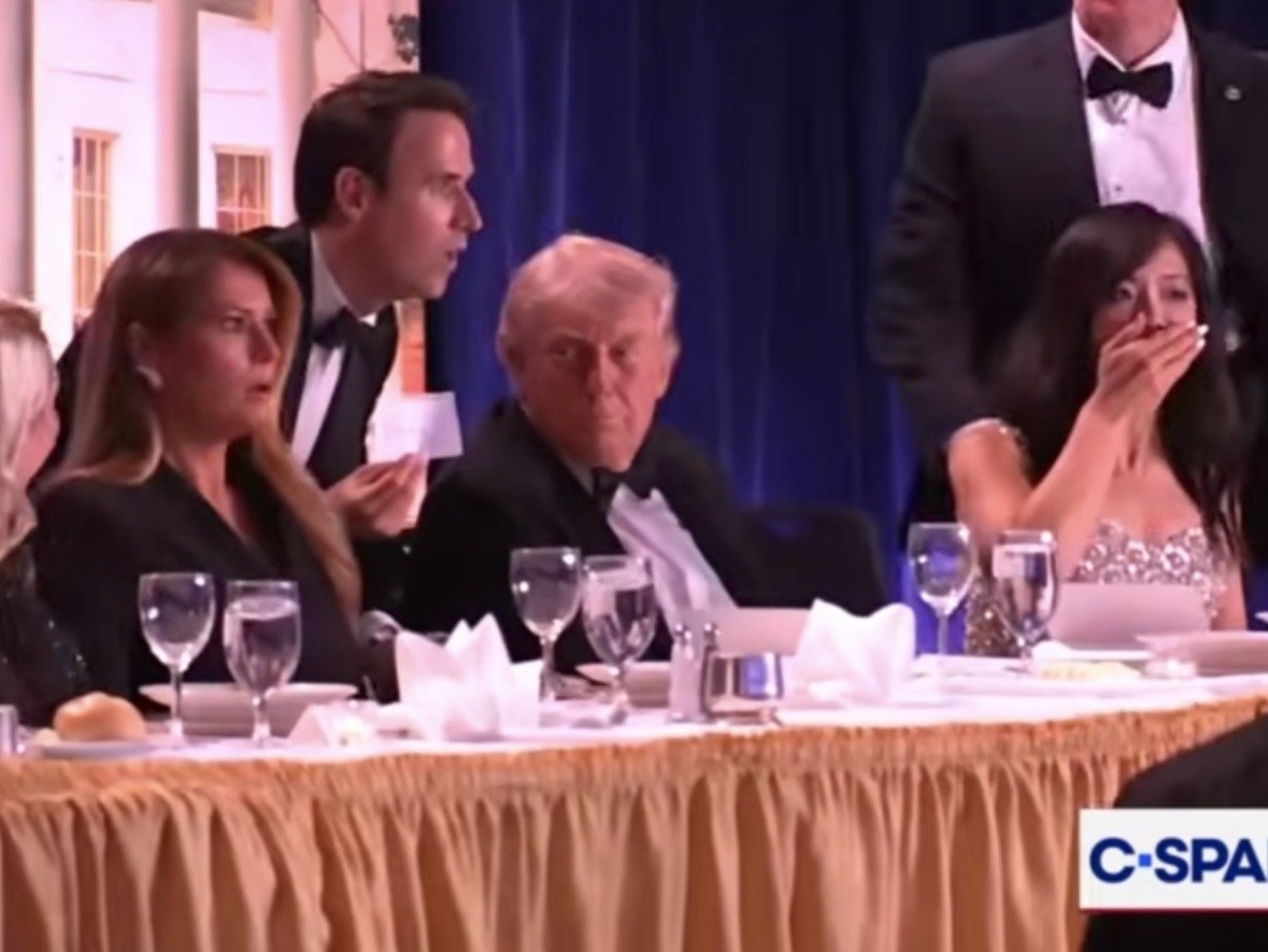 Former President Donald Trump seated at a formal dinner, surrounded by guests in elegant attire, with a tense atmosphere evident among the attendees.