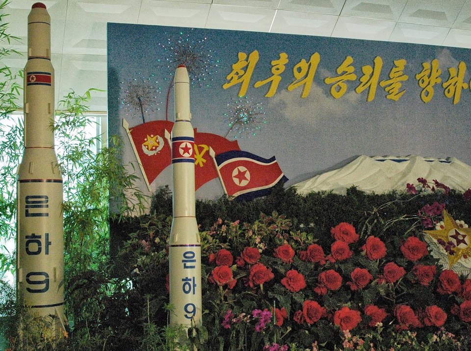 North Korean missile display surrounded by flowers and flags, symbolizing national pride and military capability.