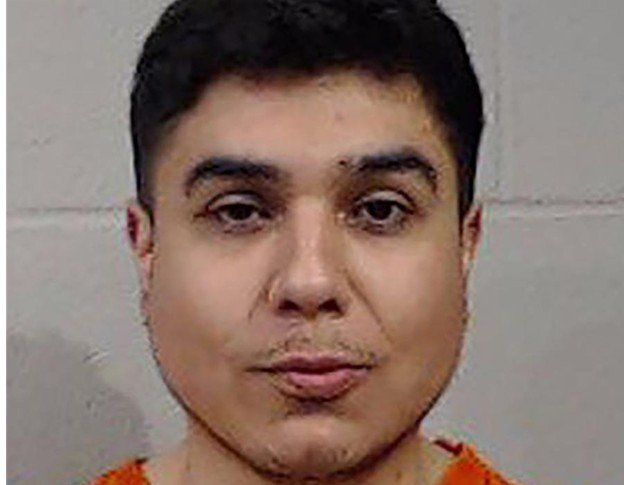 Mugshot of a man wearing an orange prison uniform against a neutral background, highlighting his facial features and expression.