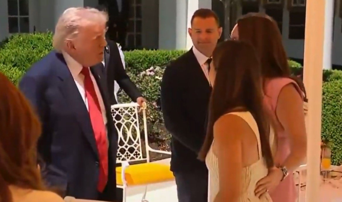 Donald Trump engages in conversation with several individuals at a social gathering in an outdoor setting.