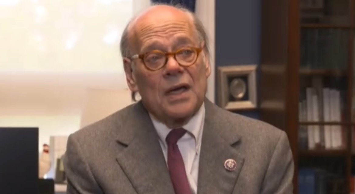 A man with glasses and a gray suit speaks in an office setting, emphasizing key political issues.