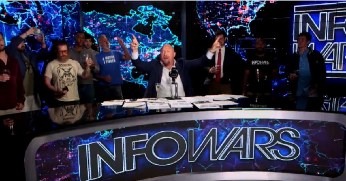 Alex Jones leads a lively discussion on the Infowars set, surrounded by enthusiastic supporters, with a digital map backdrop.