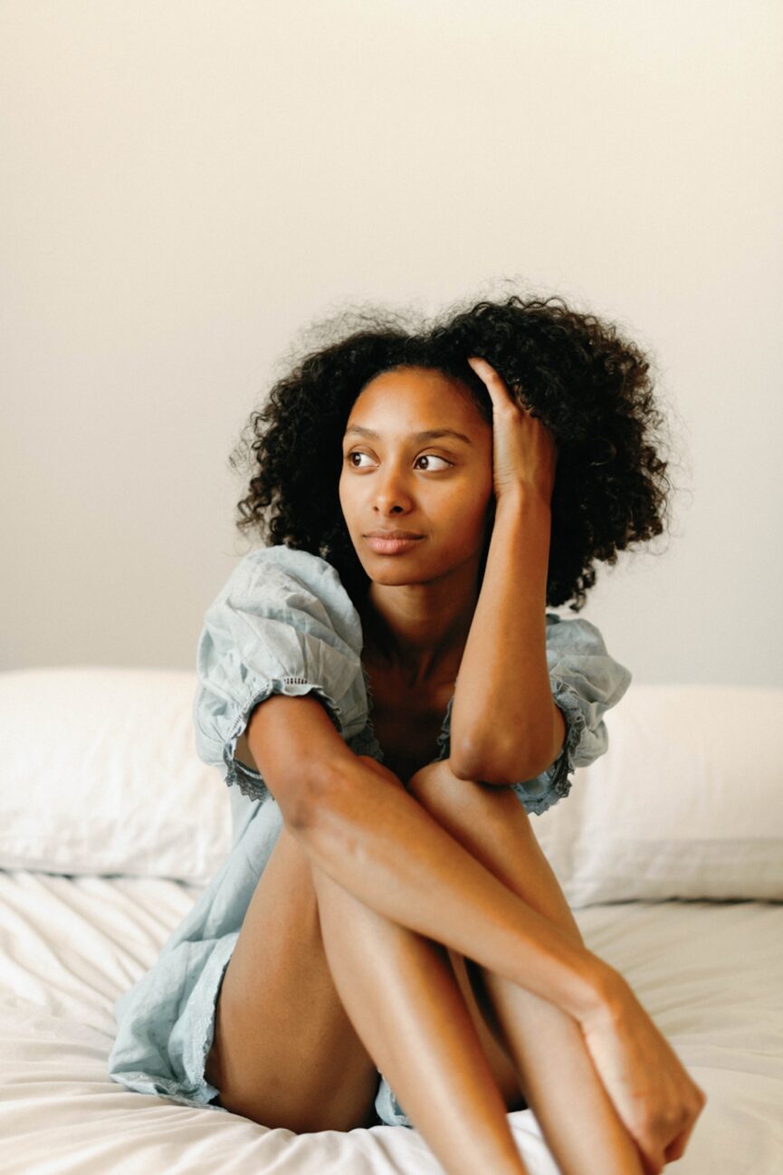 Woman sitting on bed wearing green nightgown.