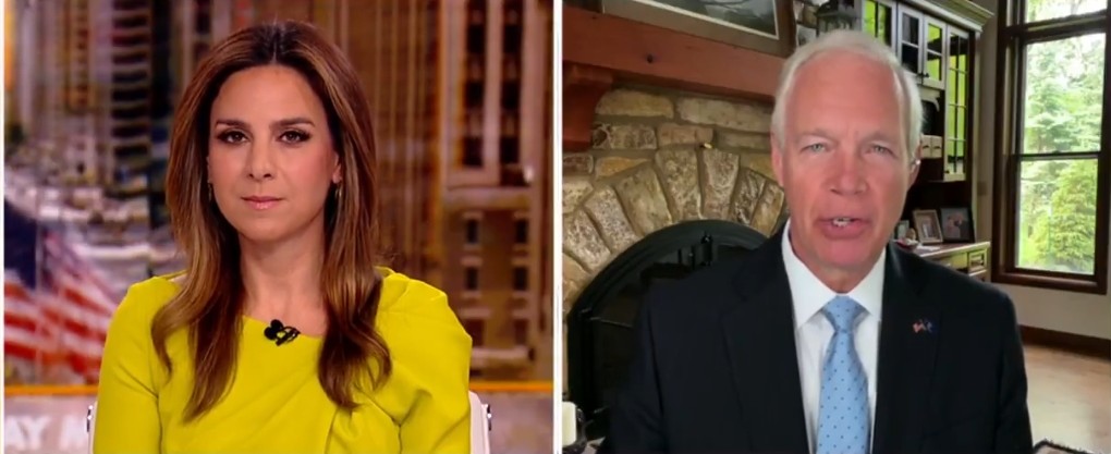 News segment featuring a female host in a bright yellow dress and a male guest in a suit discussing current events, with a cozy background setting.