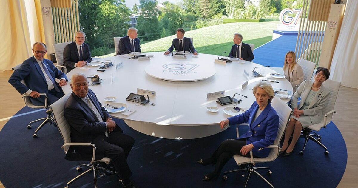 Leaders of the G7 summit gather around a circular table in a scenic outdoor setting, discussing global issues and cooperation.