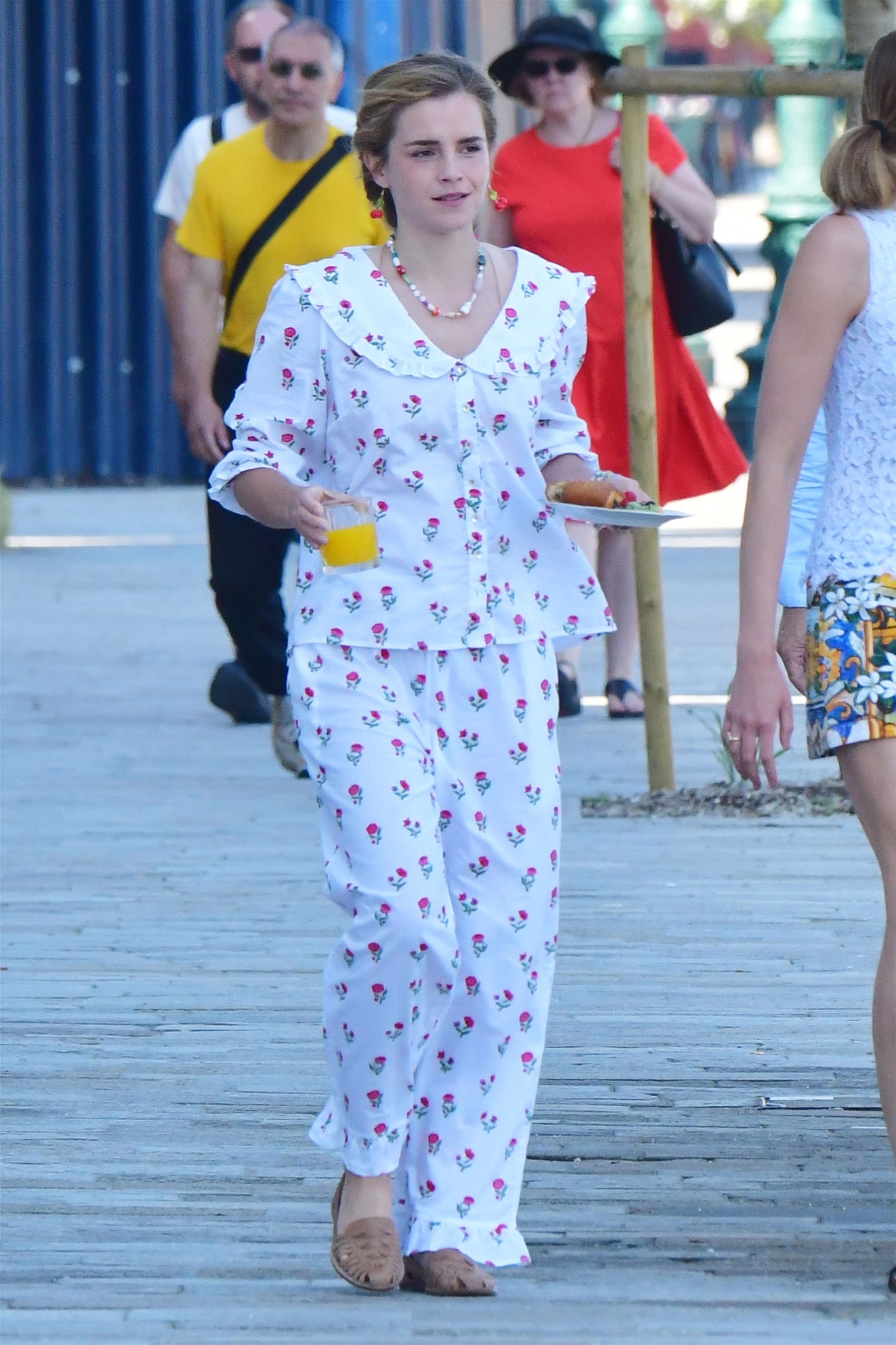 Emma Watson in a cherry-printed outfit and red cherry drop earrings carrying a breakfast plate while walking in Venice with a friend.