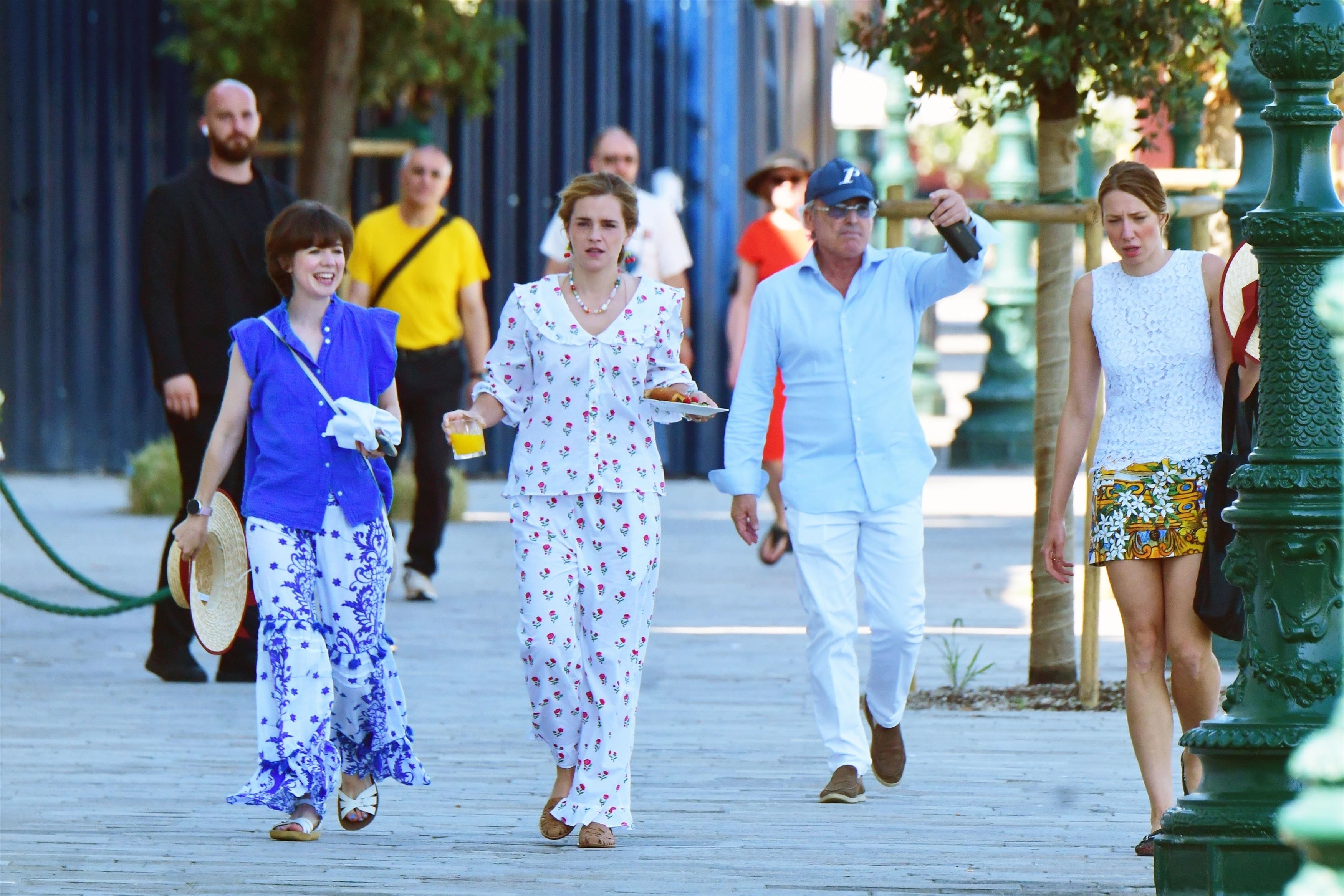 Emma Watson in a cherry-printed outfit and red cherry drop earrings carrying a breakfast plate while walking in Venice with a friend.
