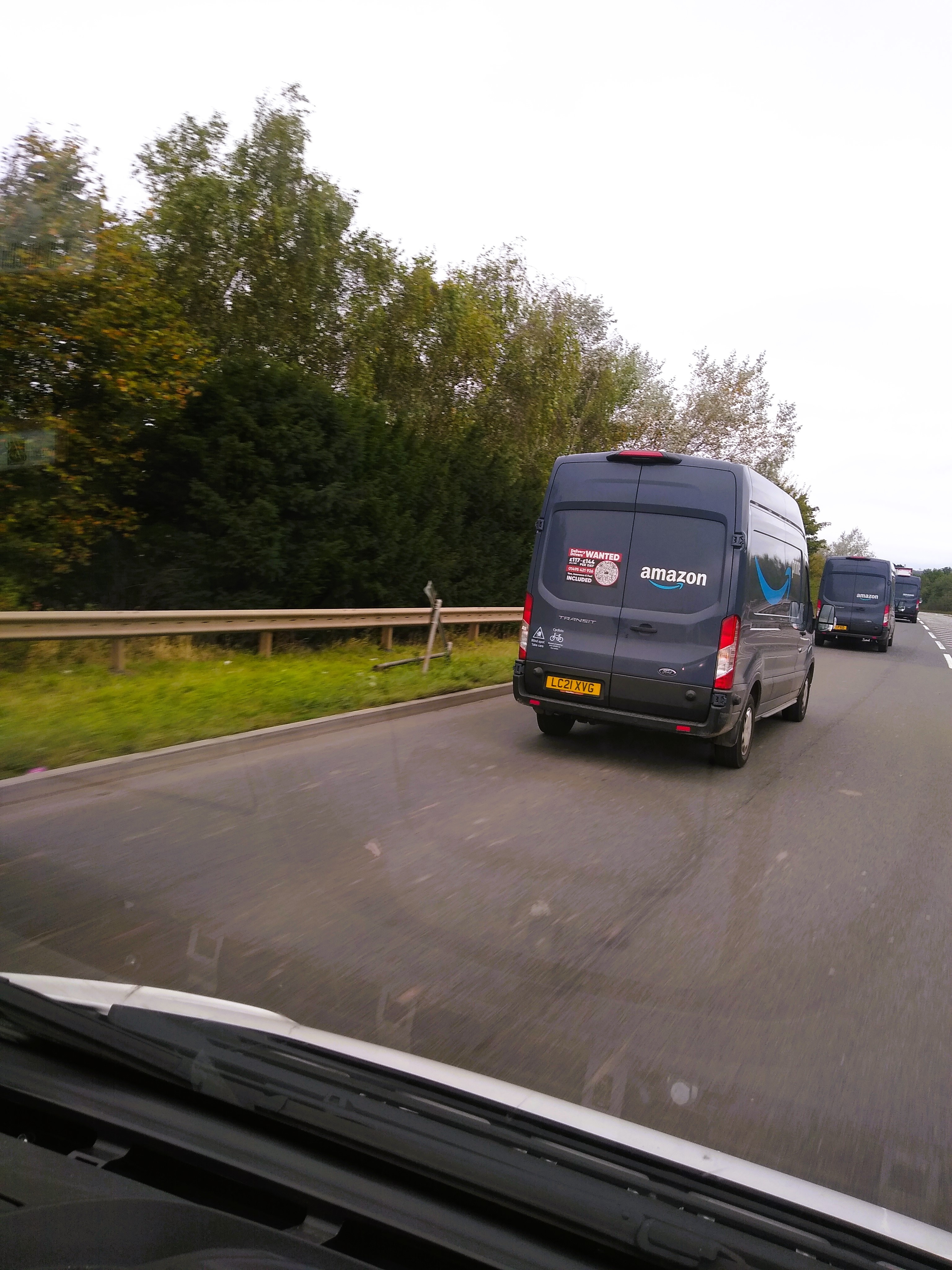 Rear view of Amazon-branded Ford Transit vans driving along a UK motorway, seen from inside a following vehicle.