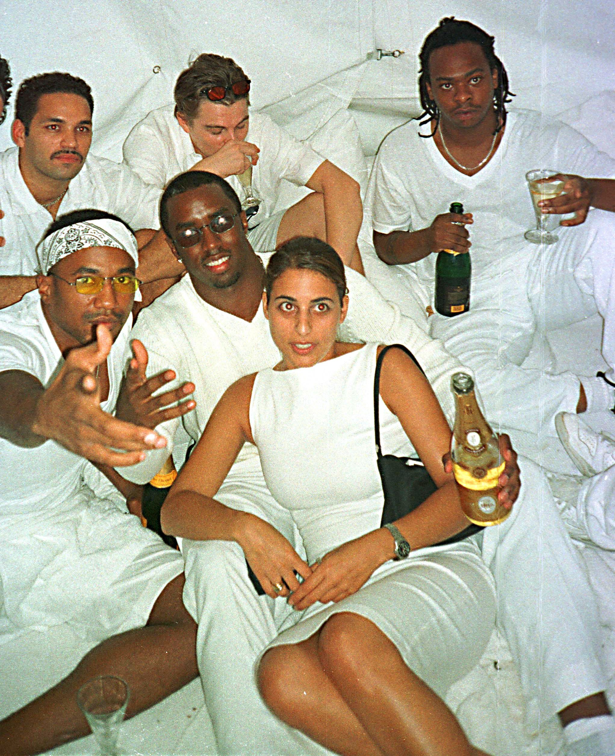 Group of people in all-white outfits lounging together at a party, holding champagne bottles and glasses.
