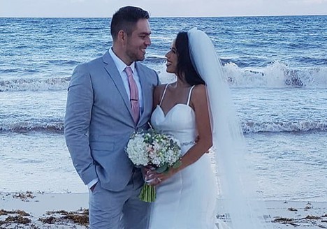 Bride and groom smiling together on a beach, with waves in the background, capturing a romantic wedding moment.