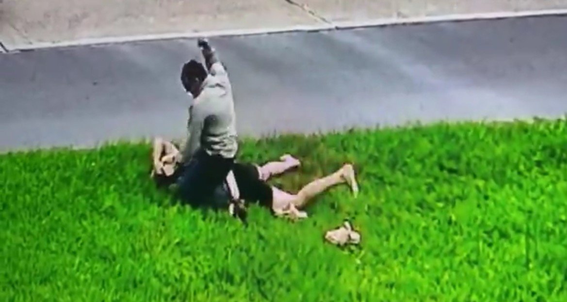 A man is seen attacking another individual on a grassy area near a road, captured by surveillance footage.