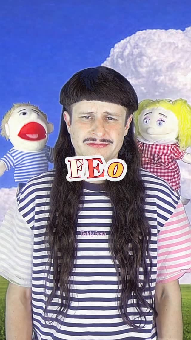 Person in striped shirt and long dark wig holding two hand puppets against a blue sky background, with the text 'FEO' overlaid.