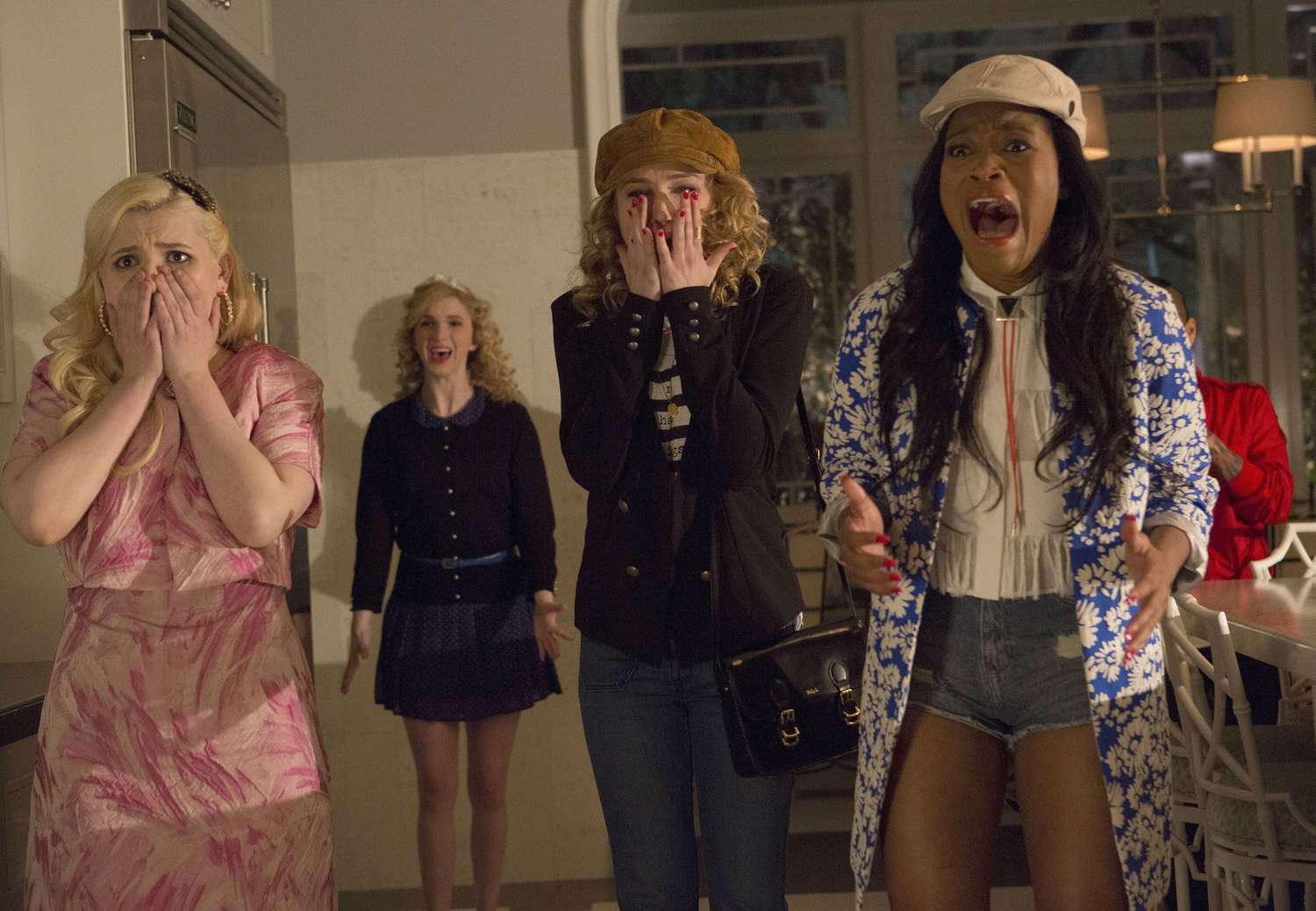 Four women reacting with shock and horror indoors, some covering their mouths and one screaming, in a TV scene.