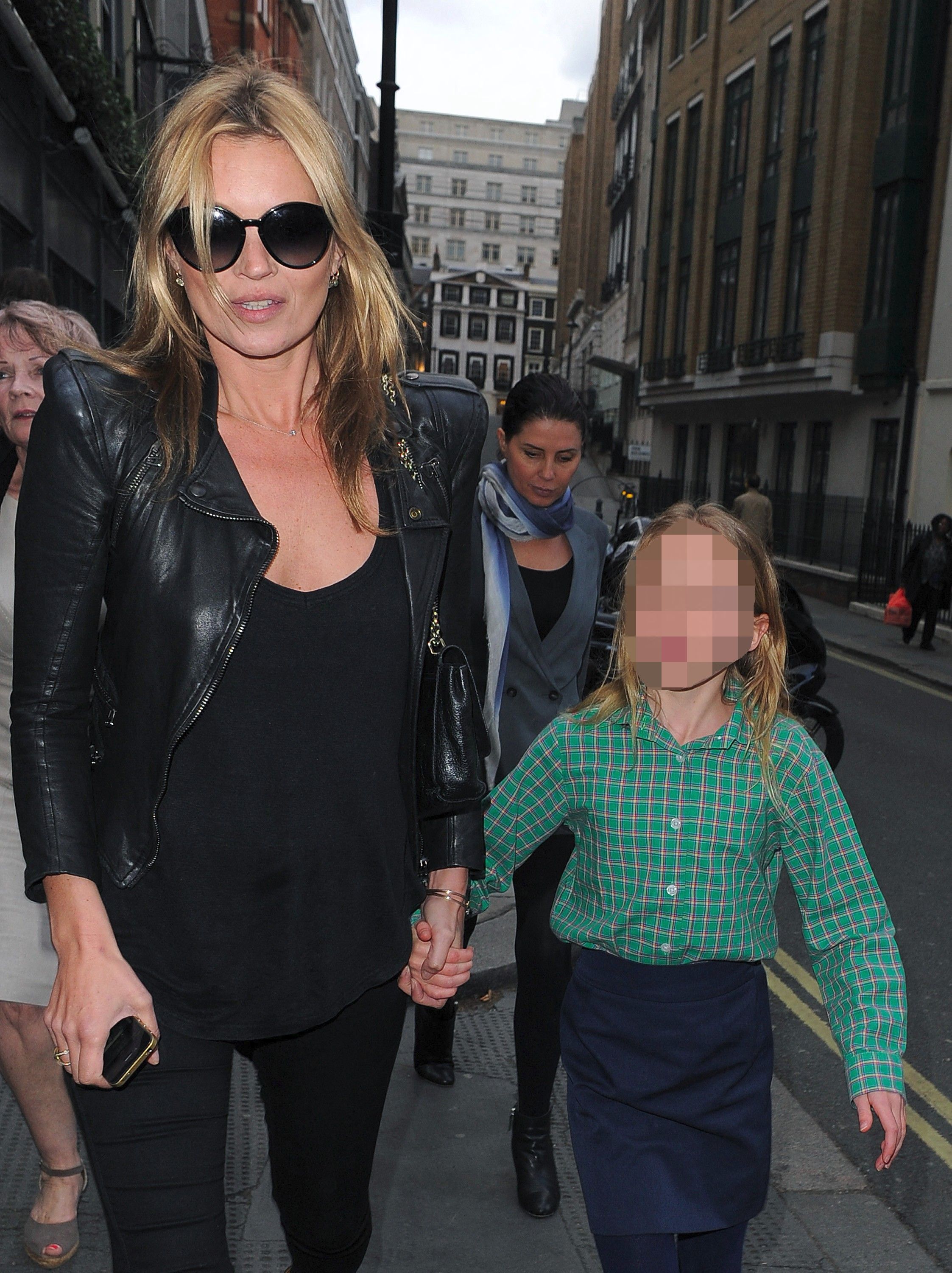 Kate Moss in a black leather jacket and sunglasses walks hand-in-hand with a young blonde girl in a green plaid shirt on a London street.
