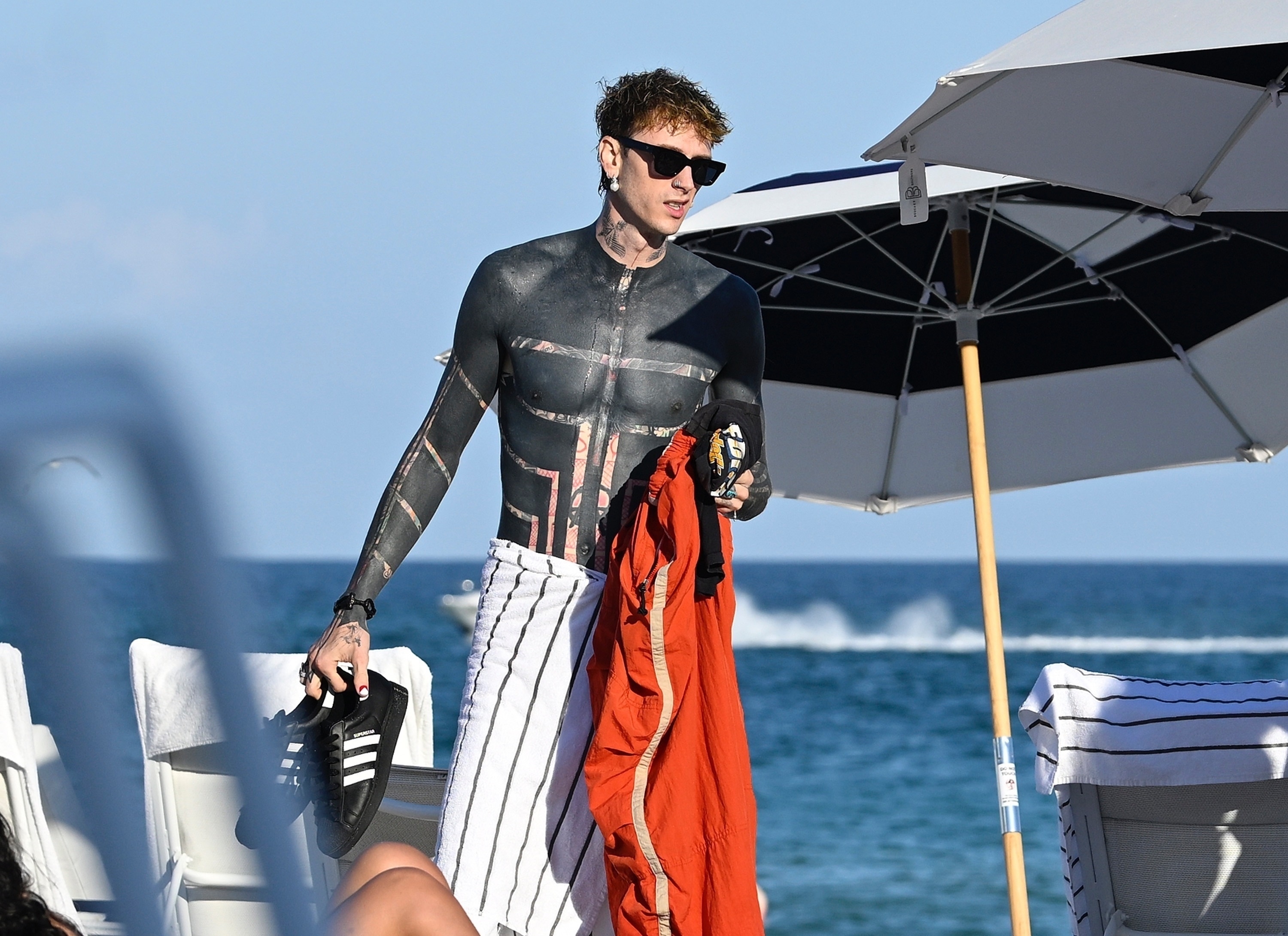 Machine Gun Kelly shirtless on a Miami beach with a group of friends and women