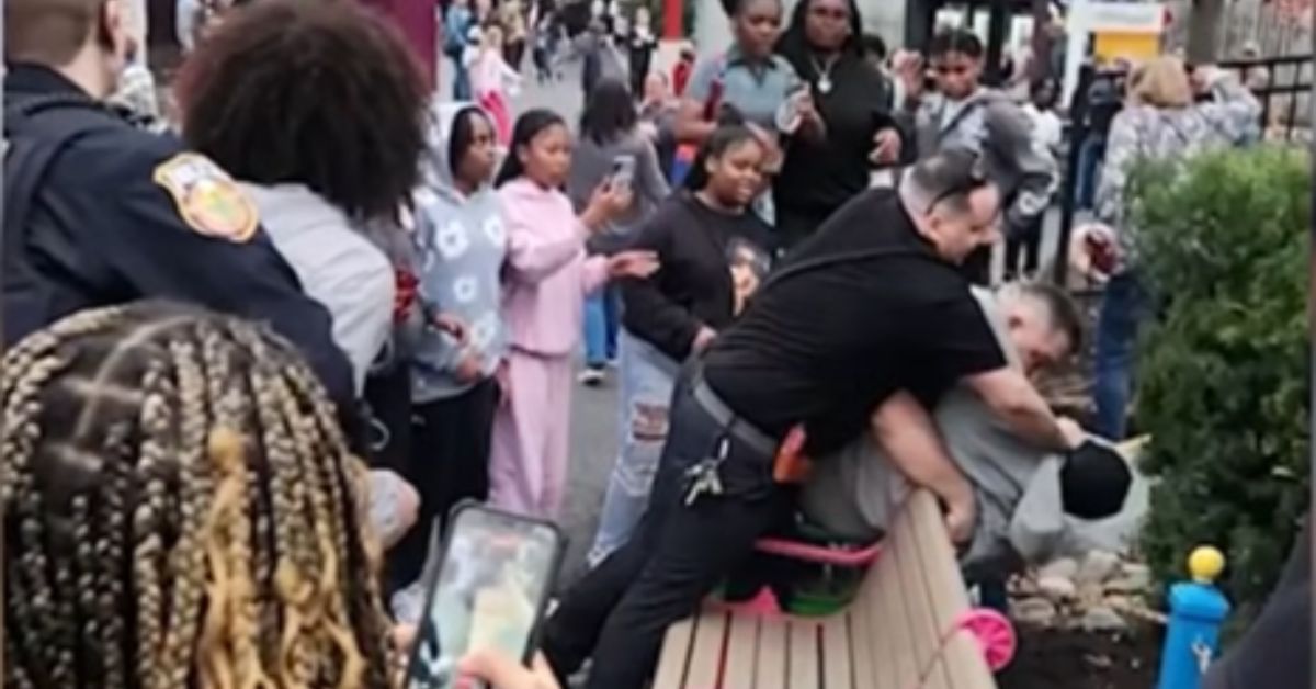 A police officer restrains an individual on a bench as a crowd of onlookers records the incident at a public event.