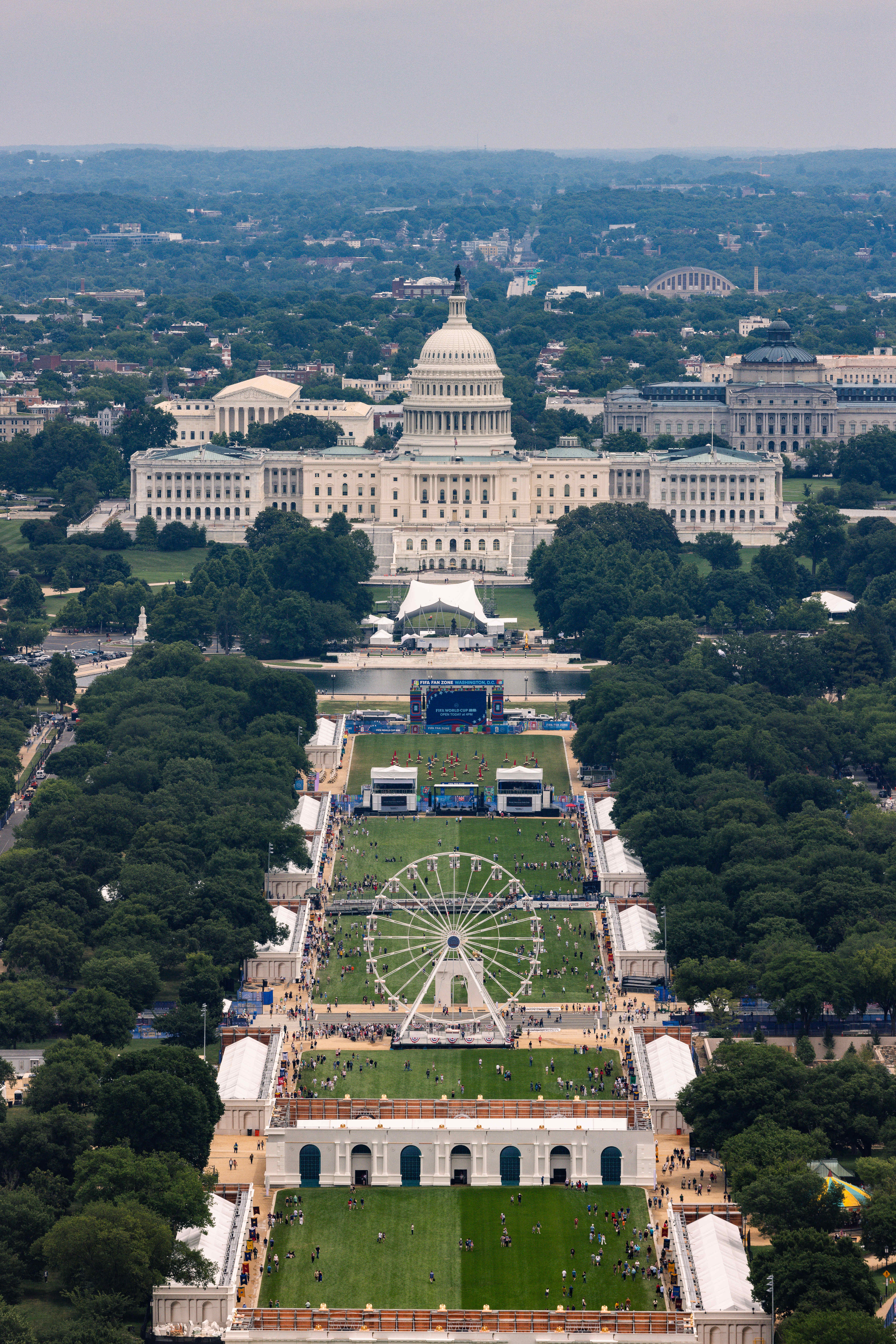 Aerial view of the Great American State Fair on the National Mall, with a large Ferris wheel in the foreground and the U.S. Capitol in the background