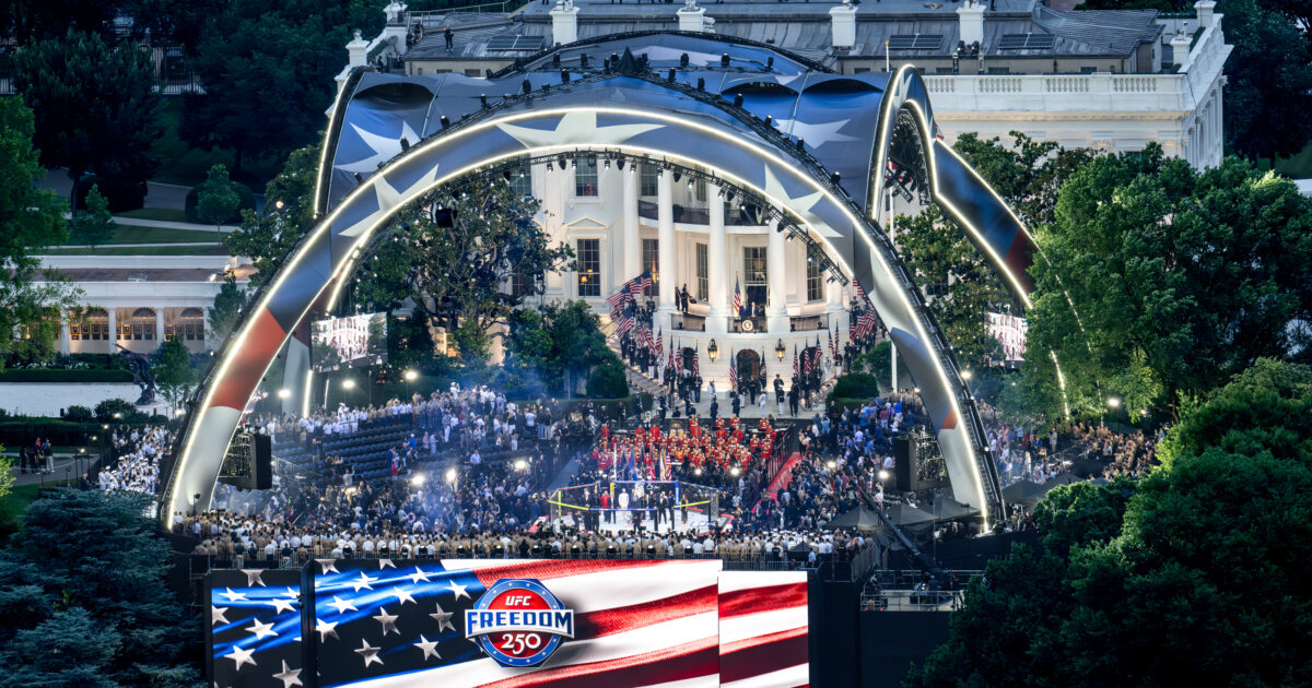 Aerial view of a large crowd at the White House celebrating the UFC Freedom 250 event, featuring a stage, American flags, and vibrant lighting.