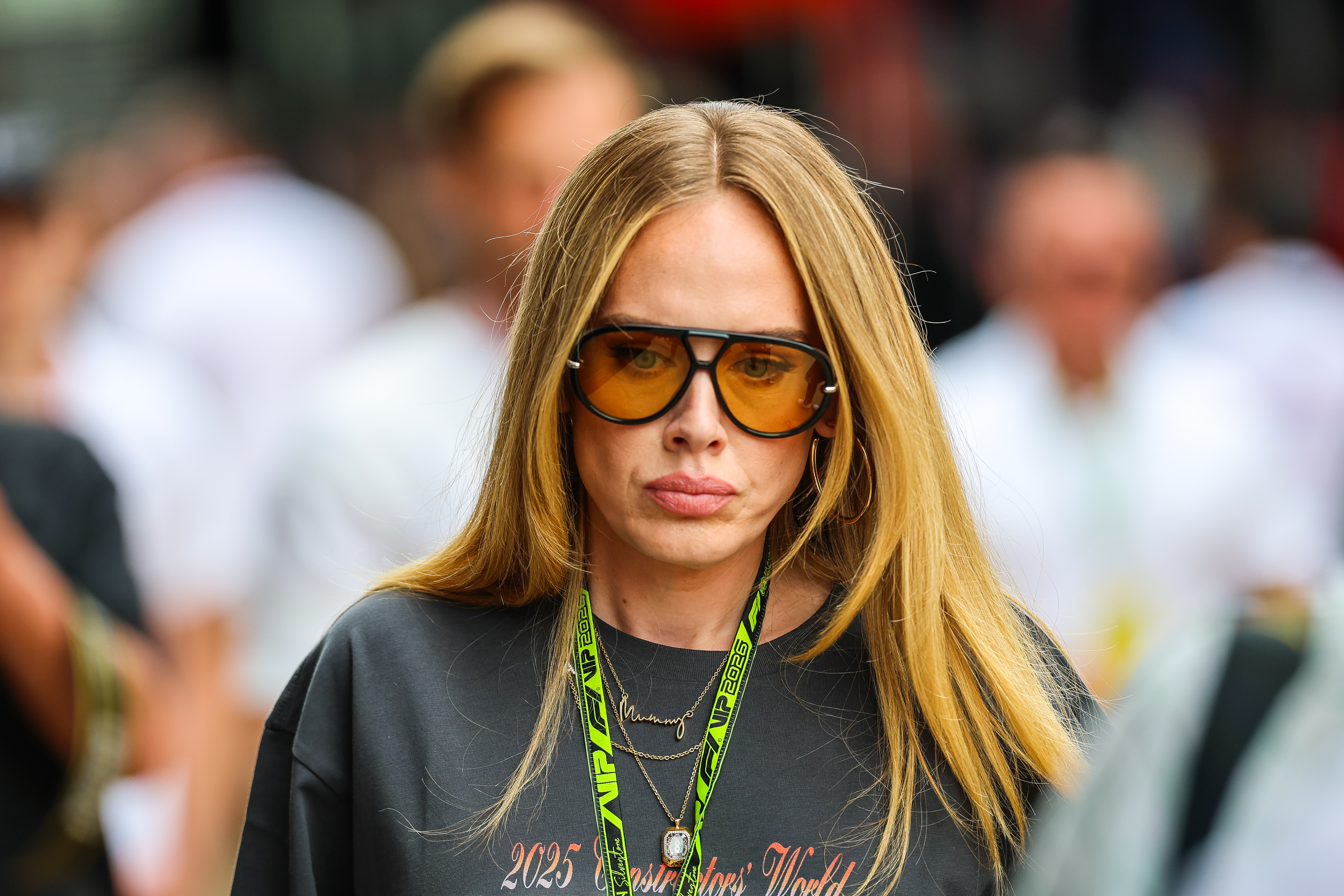 Close-up portrait of Adele in sunglasses and a dark F1 graphic tee, with layered gold necklaces including one spelling 'Mummy.'