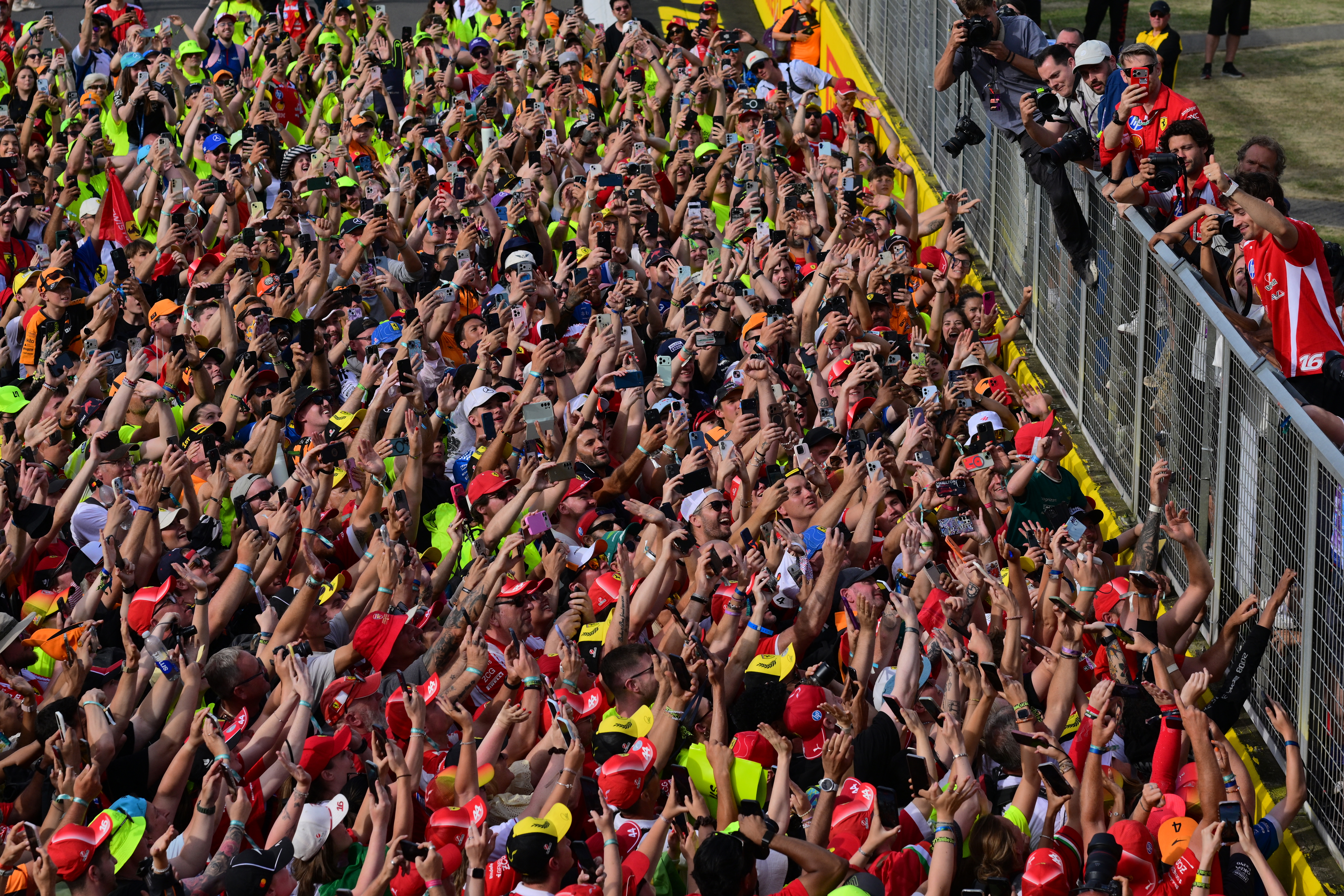 Massive crowd of Formula 1 fans with arms and phones raised on the Silverstone circuit after the British Grand Prix race.