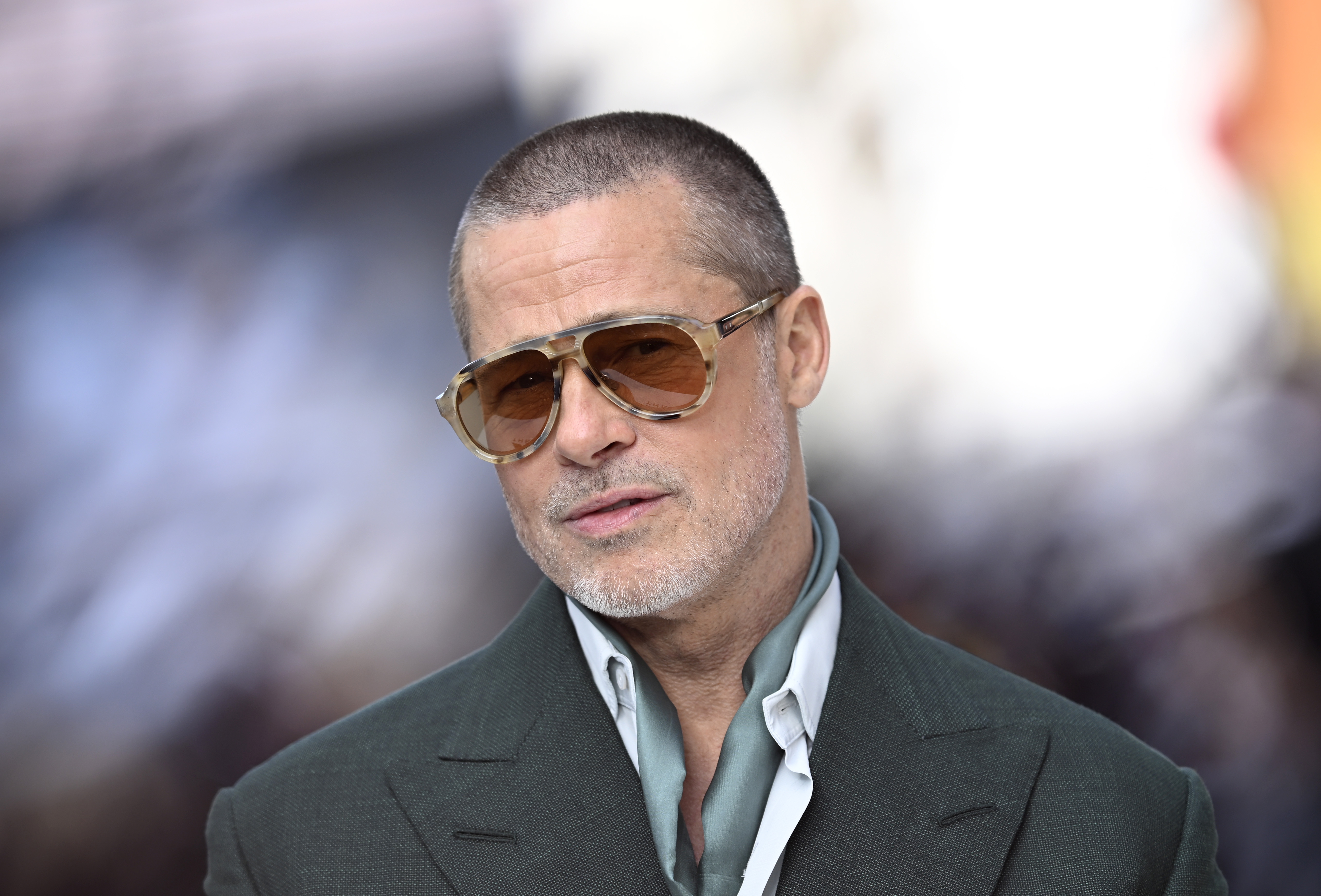 Brad Pitt wearing tinted aviator sunglasses and a dark green suit jacket at a movie premiere.
