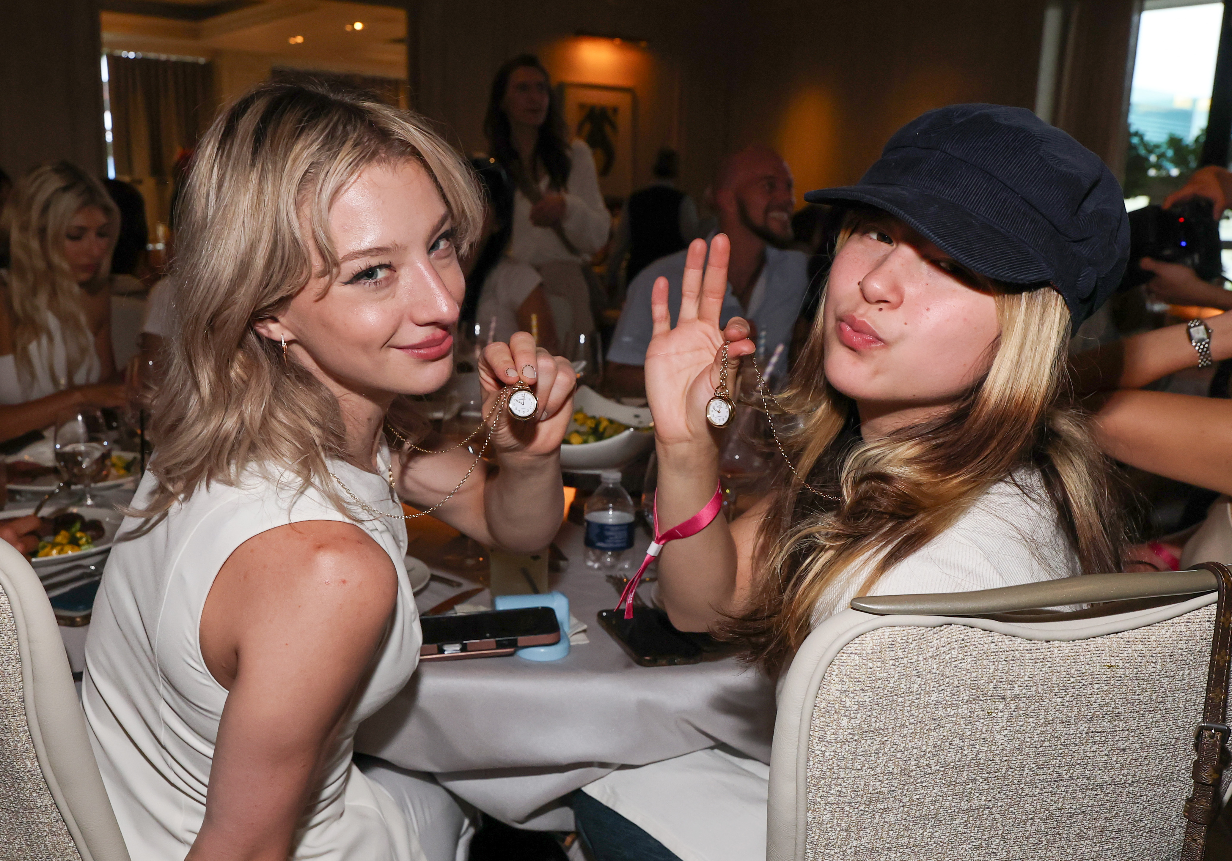 Figure skaters Amber Glenn and Alysa Liu showing off Shinola clock necklaces gifted by Flavor Flav at a Las Vegas athlete dinner