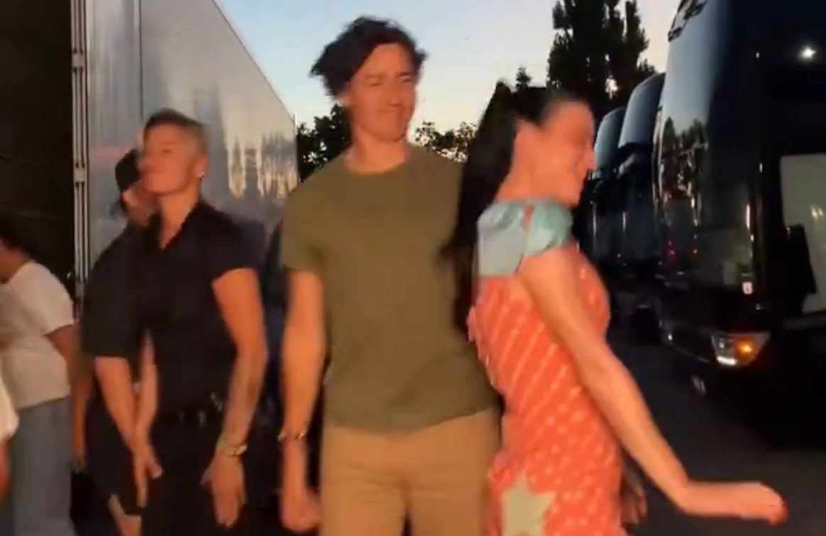 Group of people dancing outdoors near large trucks during sunset, showcasing lively expressions and colorful outfits.