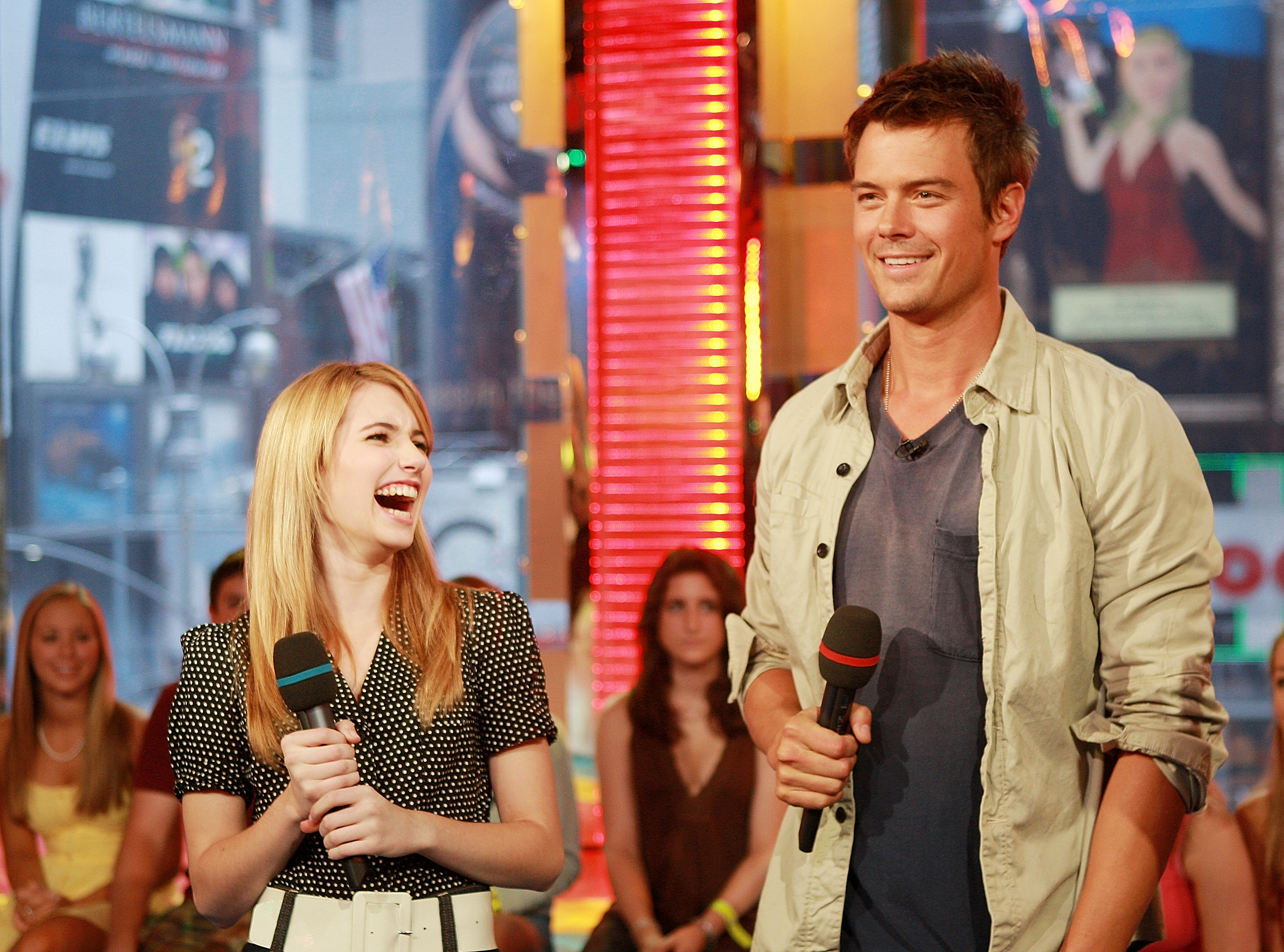 Emma Roberts laughing and Josh Duhamel smiling while holding microphones on the set of MTV's Total Request Live.