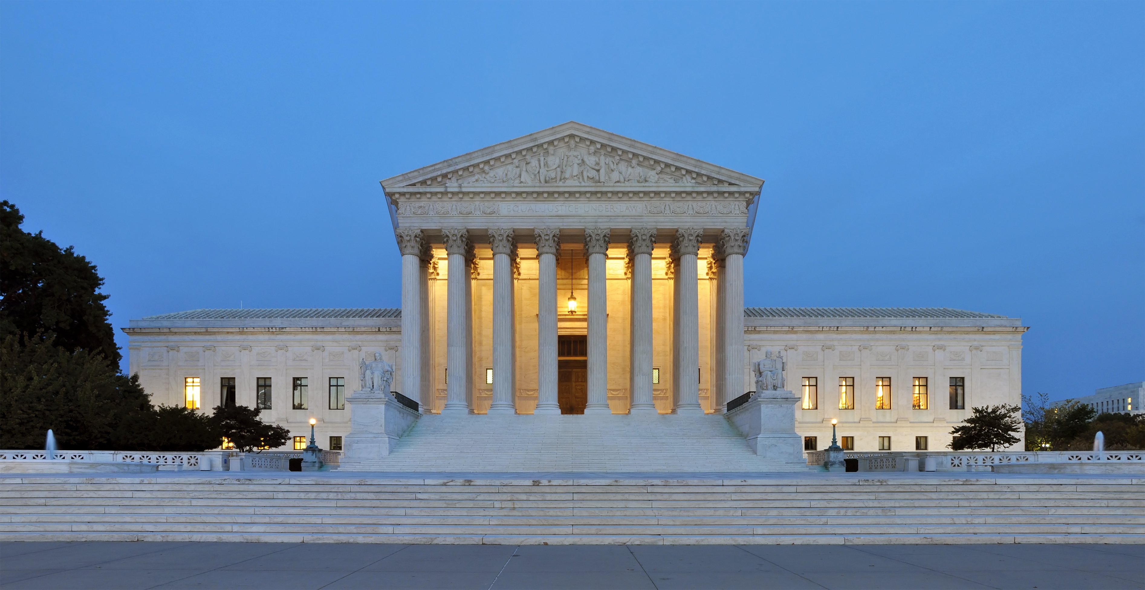 The exterior of the U.S. Supreme Court building illuminated at dusk, showcasing its neoclassical architecture and iconic columns.