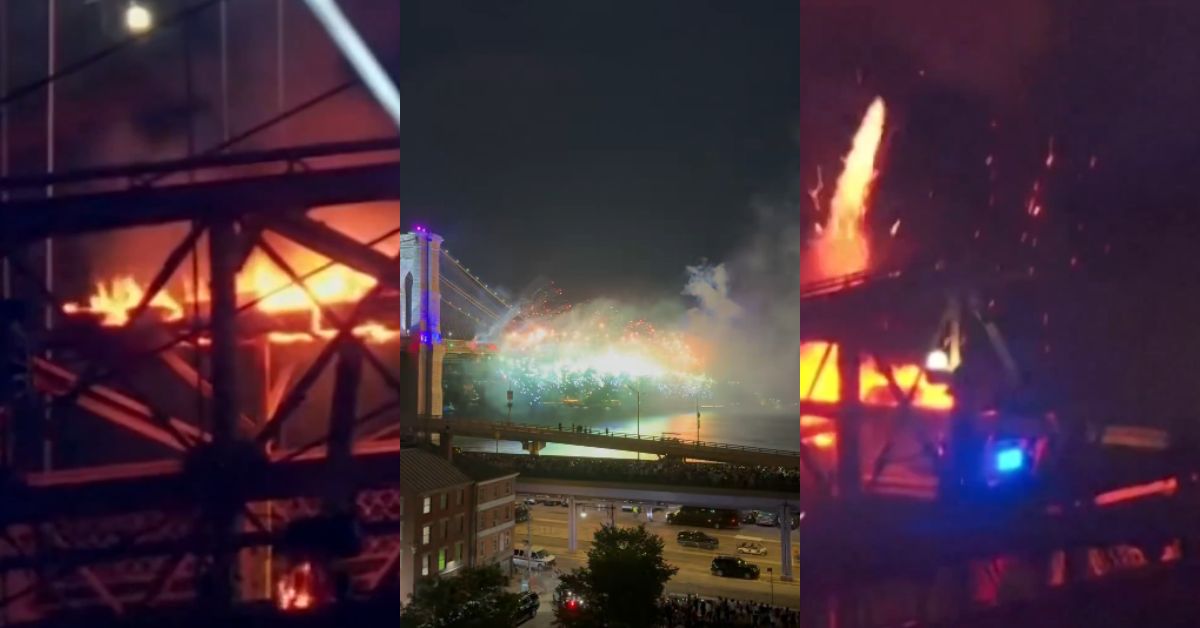 Fire erupts on a bridge at night, with bright flames and sparks visible, while crowds watch from below amidst a colorful display in the background.