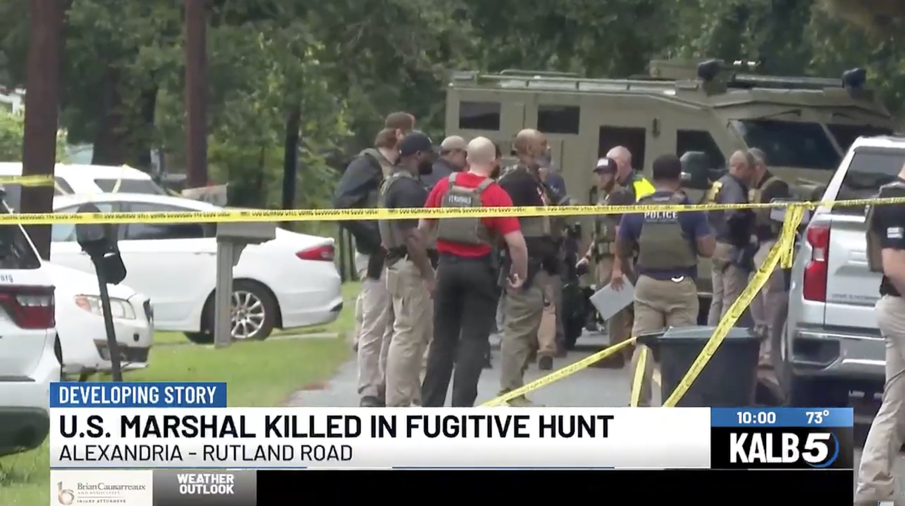 Law enforcement officials gather at the scene of a U.S. Marshal's death during a fugitive hunt in Alexandria, with police vehicles and crime scene tape visible.